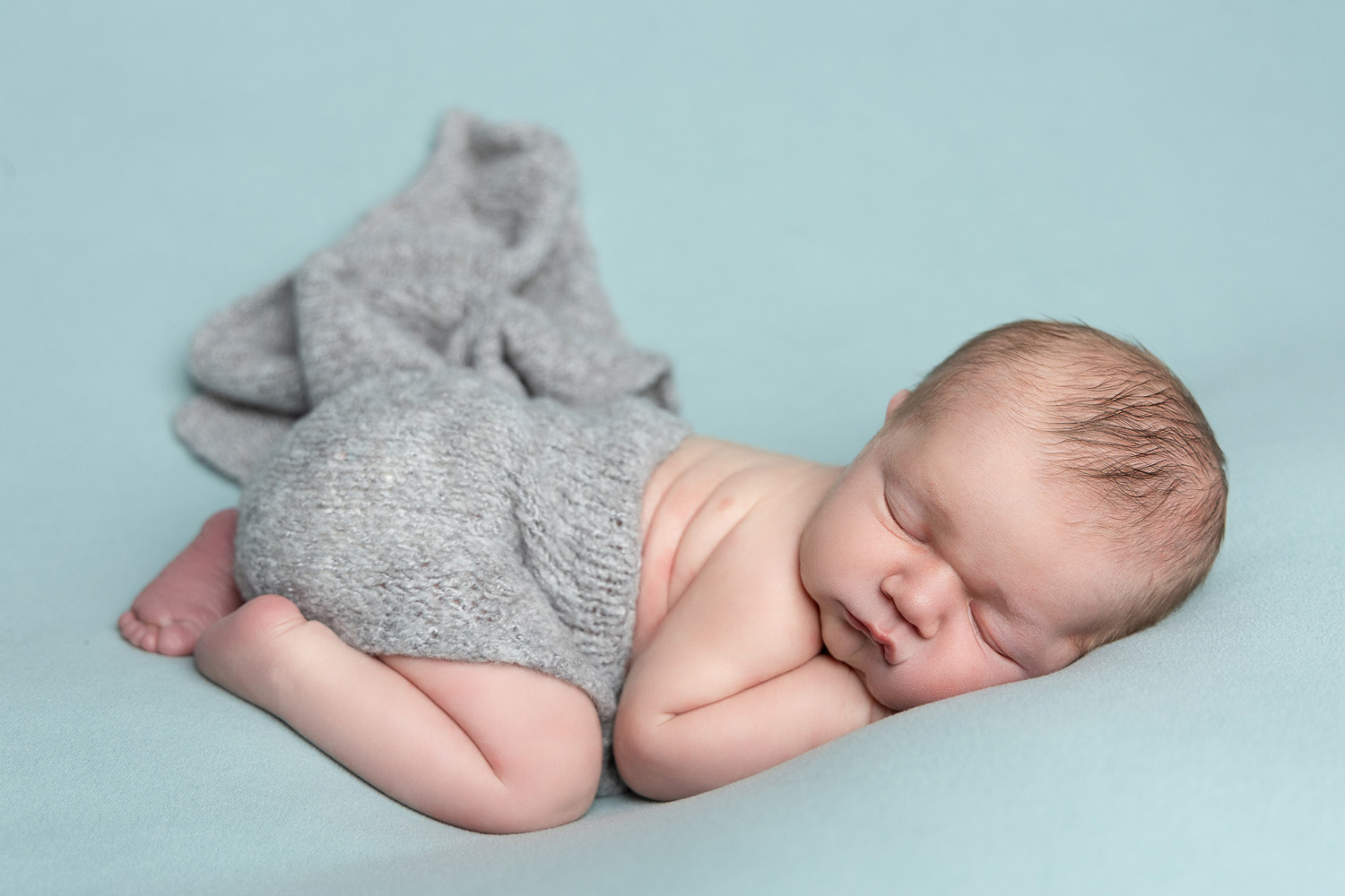 A sleeping newborn swaddled in a cream blanket, resting in a woven basket with soft textures, surrounded by gentle pastel tones. The baby’s tiny hands are visible, and the scene is serene and peaceful.