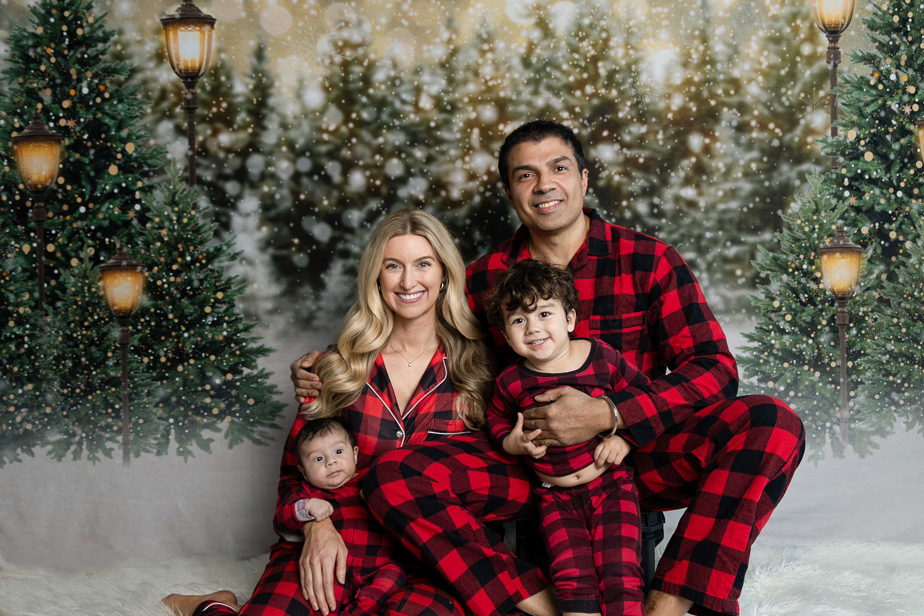 A joyful family of four, dressed in cozy holiday sweaters, laughing together on a minimal, festive set with soft golden lights and subtle Christmas decor. The background is warm and neutral, emphasizing togetherness and seasonal cheer.