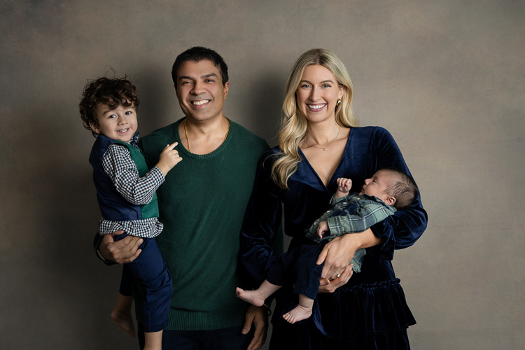 A candid moment of a young family laughing together in a sunlit park, with soft natural light and gentle pastel tones, evoking warmth and connection. The composition is balanced, with the family centered and greenery softly blurred in the background.