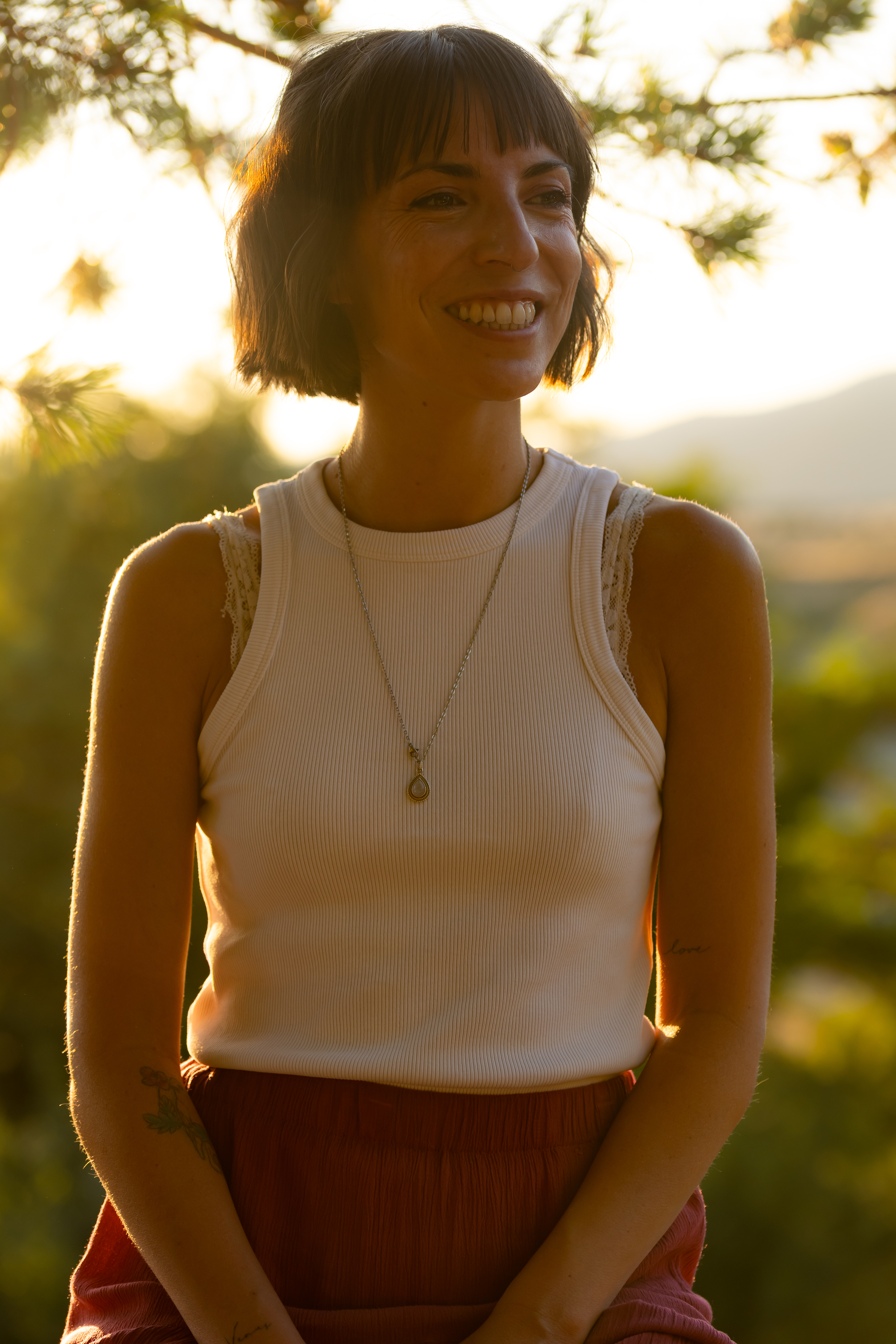 Un retrato cuadrado (1:1) de una mujer madura con cabello plateado y ojos cálidos, que lleva joyería de temática celestial y un chal azul profundo. Está sentada en un estudio suavemente iluminado lleno de libros de astrología y cartas estelares, irradiando sabiduría y cercanía.