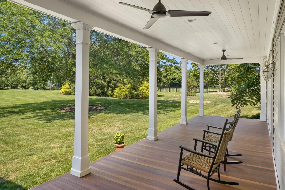 Beautiful porch with natural wood finish composite deck with wicker rocking chairs, looking out over a big lush and green backyard. A relaxing view to enjoy the warmer seasons.