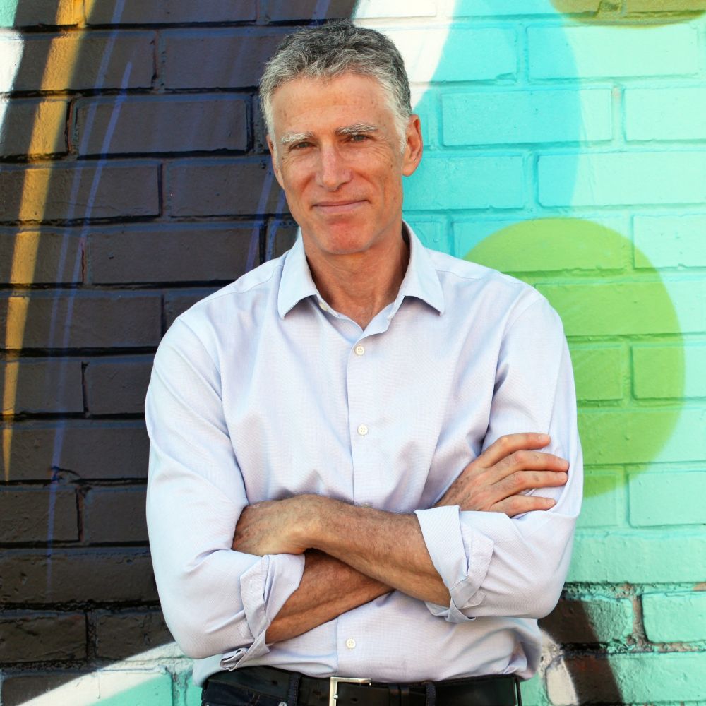 A smiling professional woman in her 40s using a tablet in a bright, modern lounge, gold and teal accents, relaxed yet focused, 3:2 aspect ratio. The setting is inviting, with plants and soft seating, conveying approachability and readiness for connection.
