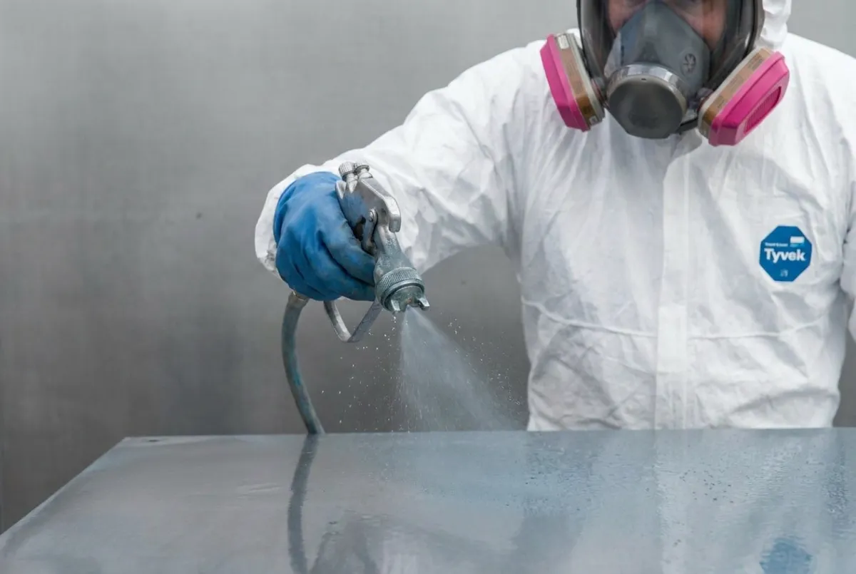 Gloved hand in white protective coveralls applying an industrial coating