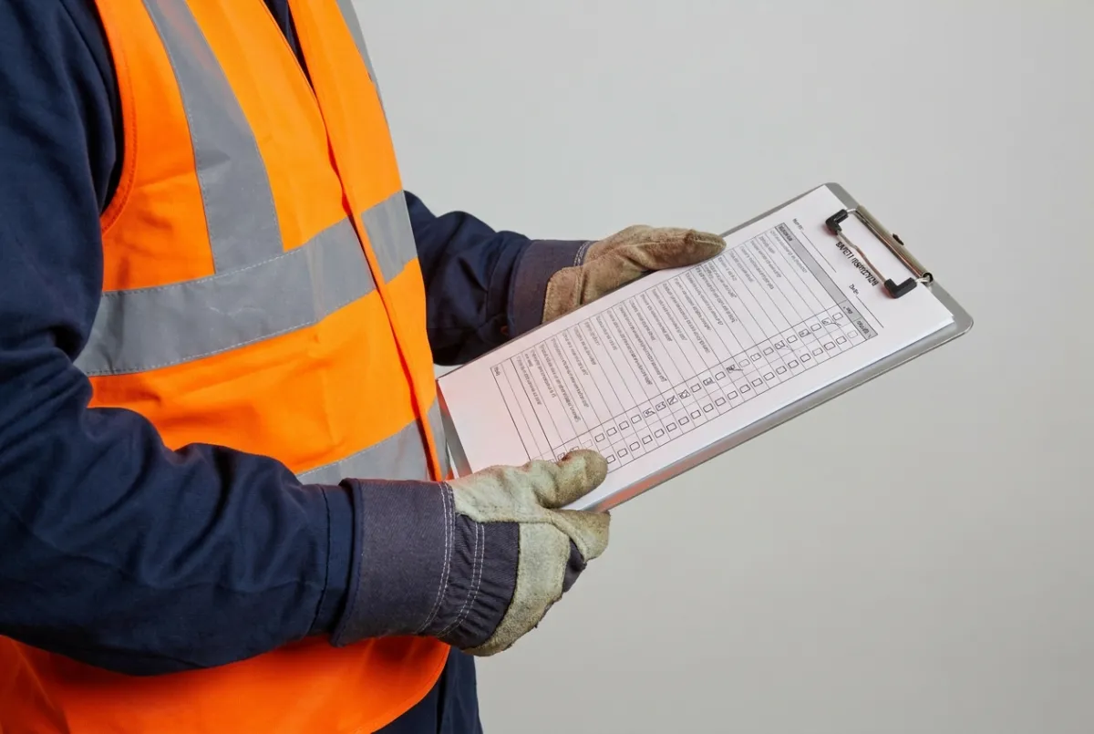 Operative in orange hi-vis PPE holding a clipboard on site
