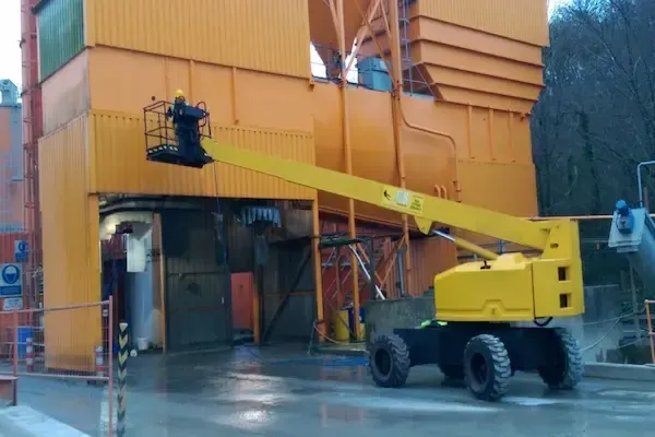 Operative in a raised cherry picker platform accessing an elevated industrial processing structure