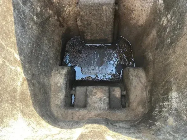 Close-up top-down view of a heavy equipment bucket with standing dark liquid, possibly oil or hydraulic fluid.