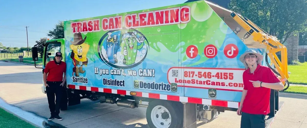 Two young men in uniform stand proudly next to a vividly branded trash can cleaning truck in a suburban setting.
