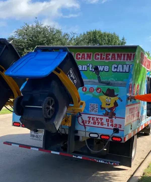 Rear view of a brightly colored garbage can cleaning truck in action, with a blue recycling bin elevated, ready for cleaning.