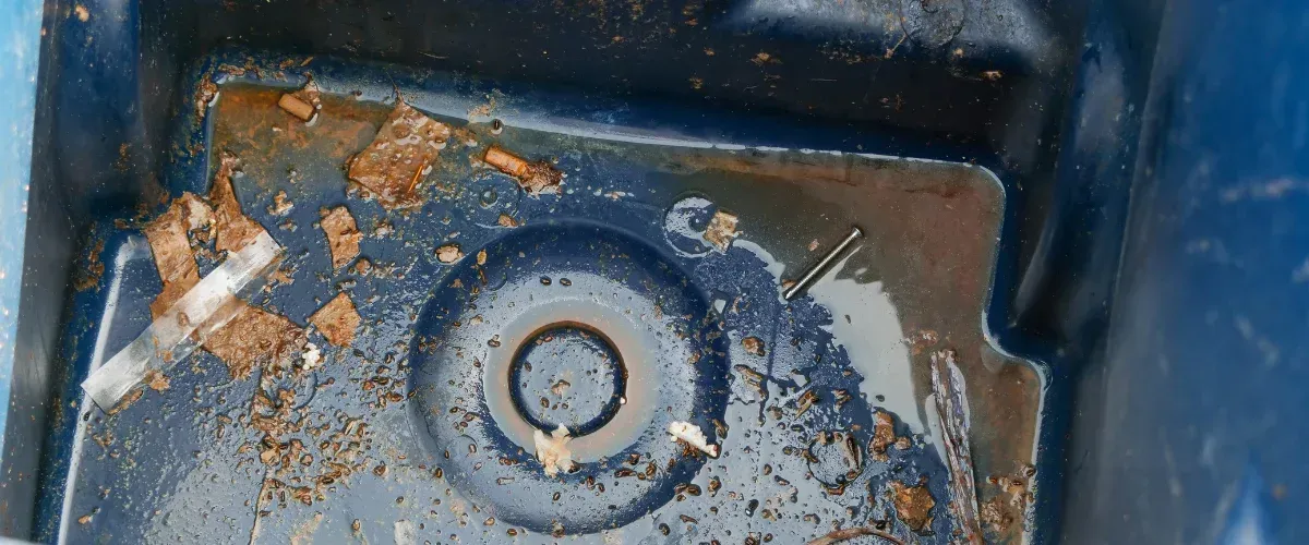 A close-up view of the dirty bottom of a blue plastic bin, covered with rusty debris and water.
