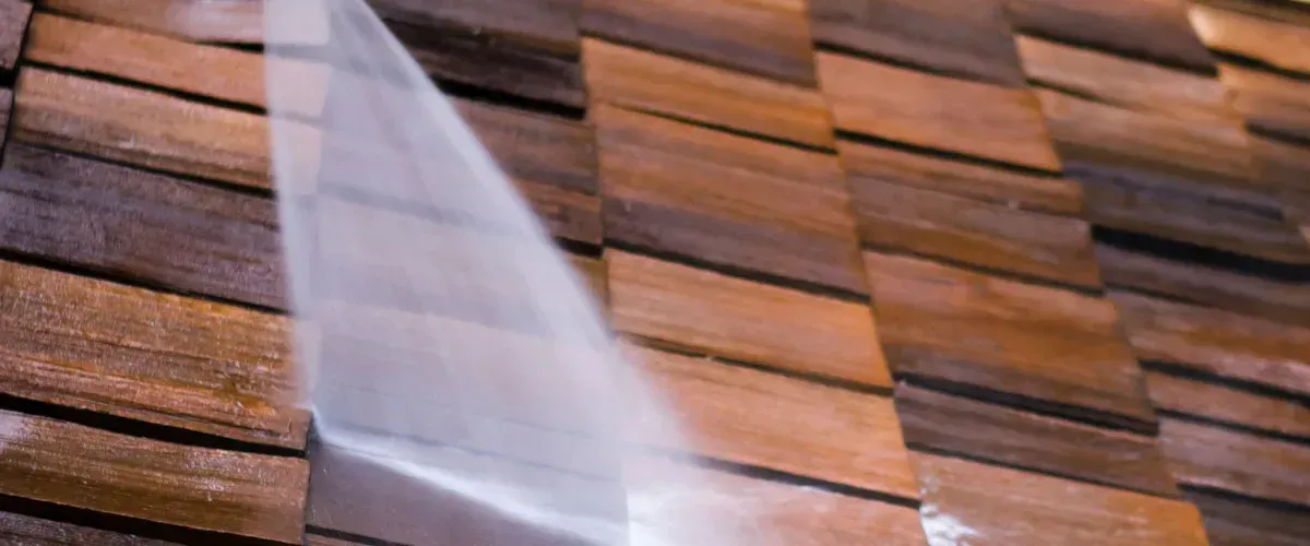 A focused shot of high-pressure water being sprayed onto rustic wooden siding, cleaning it