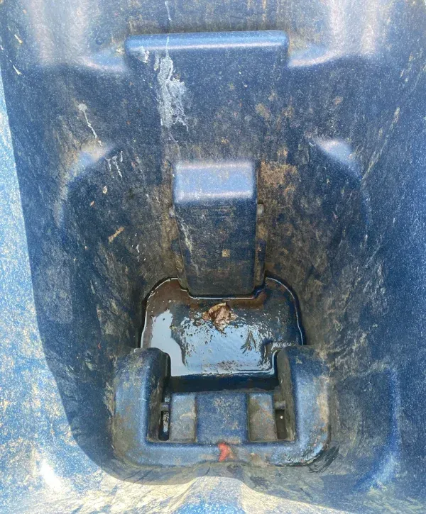A close-up, overhead view of the inside bottom of a dirty blue bin with water, mud, and debris.