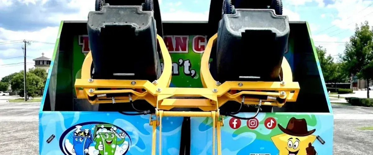 Rear view of a carnival ride or game with two black seats supported by yellow metal, and a colorful cartoon-themed base.