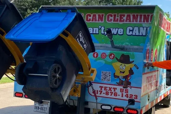 Rear view of a specialized garbage can cleaning truck lifting a blue-lidded recycling bin.