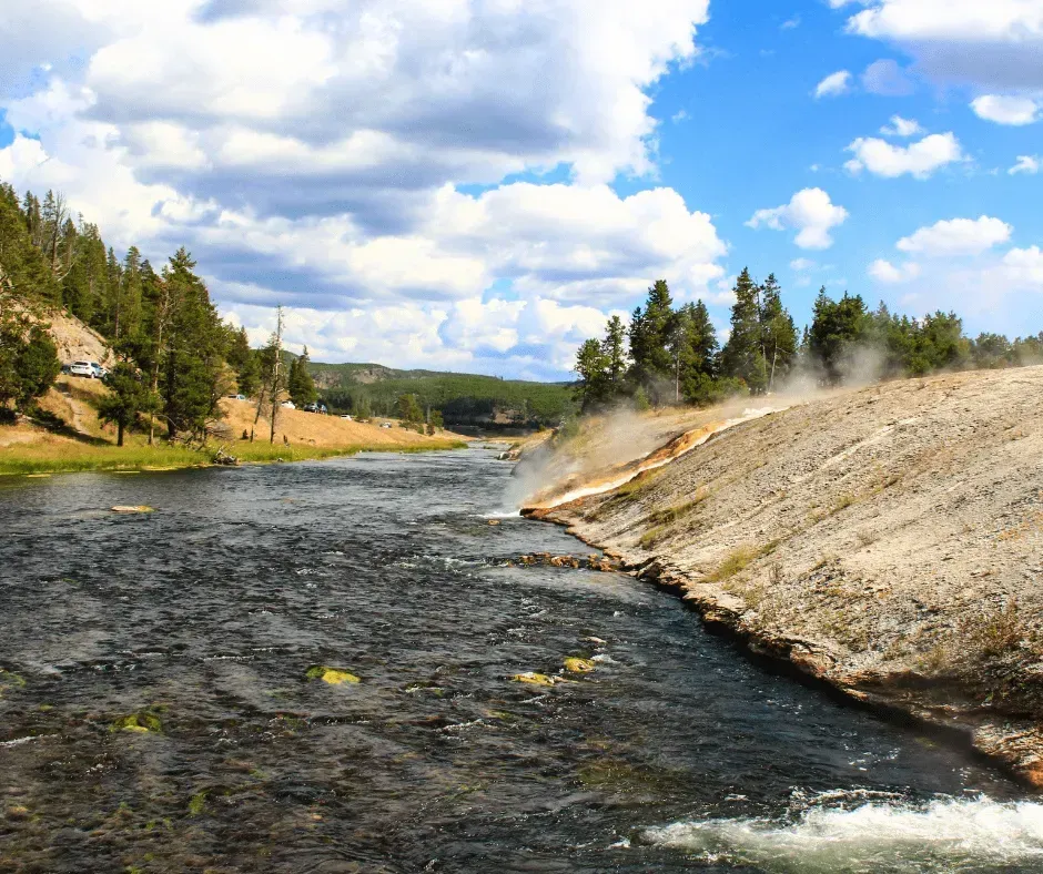 Clear rushing river with geothermal steam rising near pine forests along the Wapiti Wyoming corridor — scenic land and property for sale near Yellowstone with Wild West Real Estate Group