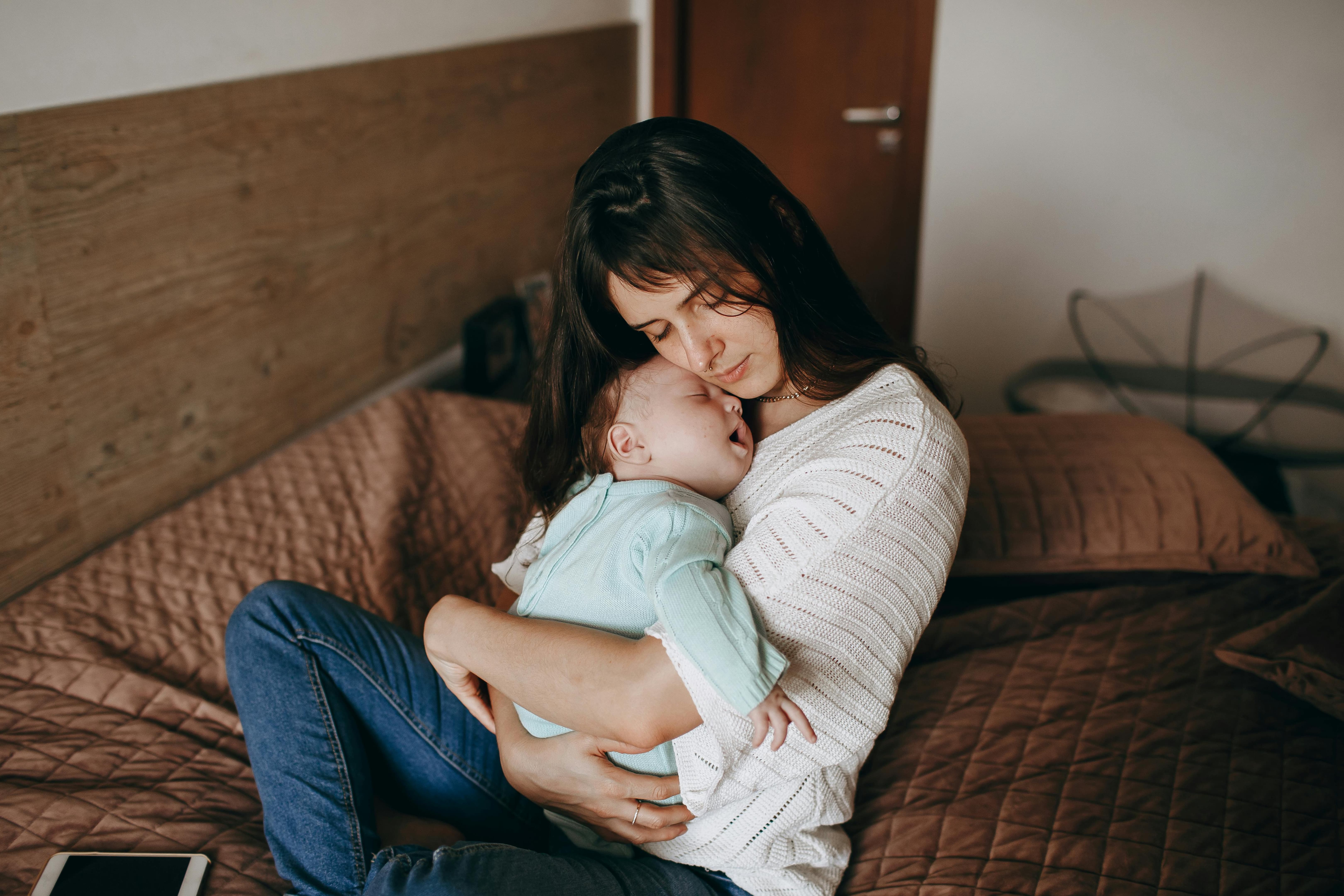 Mother comforting her baby while sitting together on a bed.