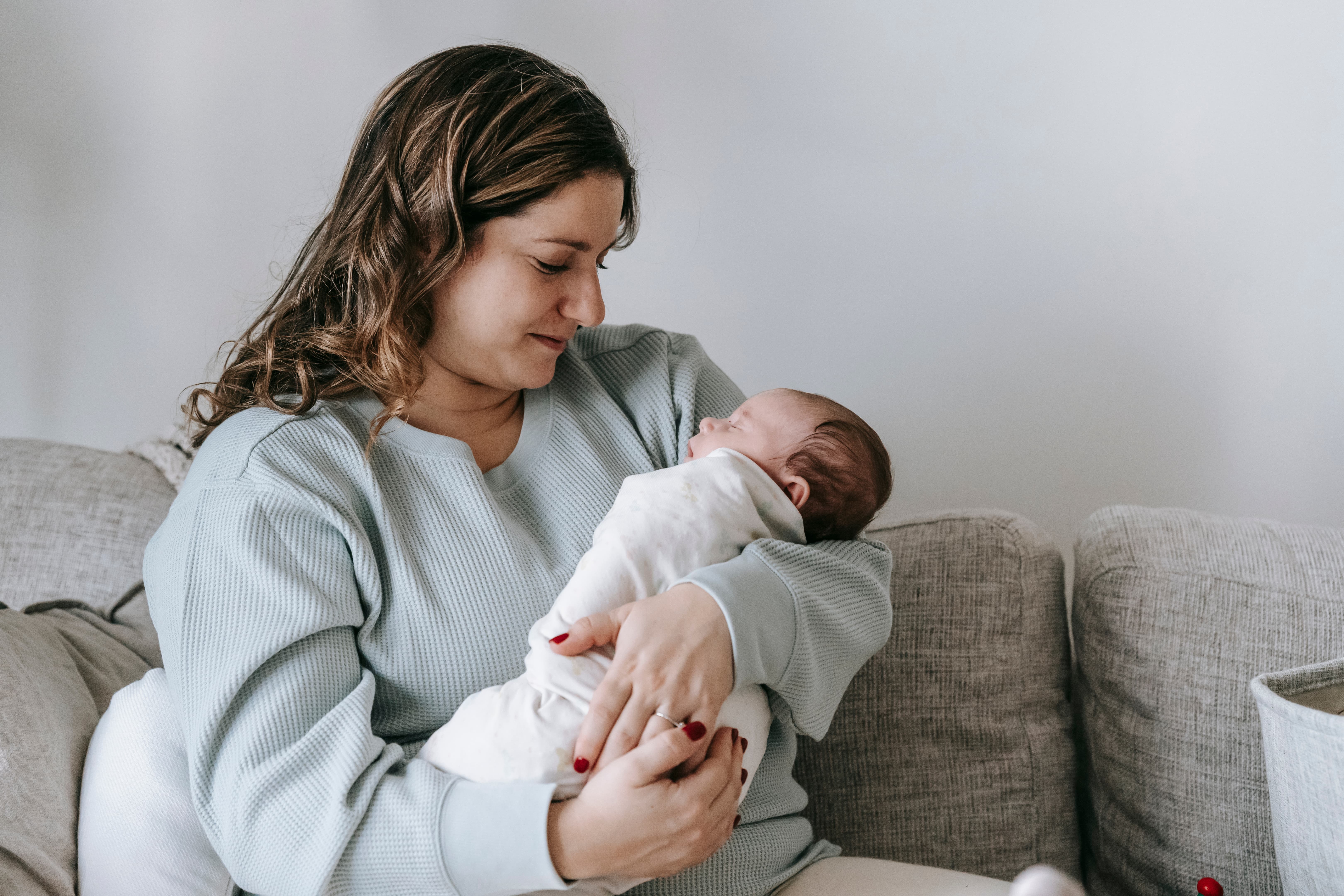 Mother holding her newborn baby while sitting on a sofa.