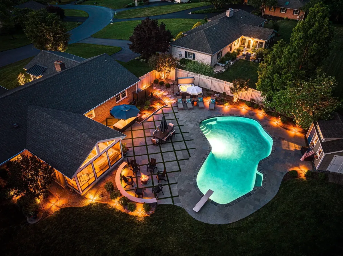 Aerial view of an illuminated backyard pool and patio created by a landscaper in Ambler, PA.