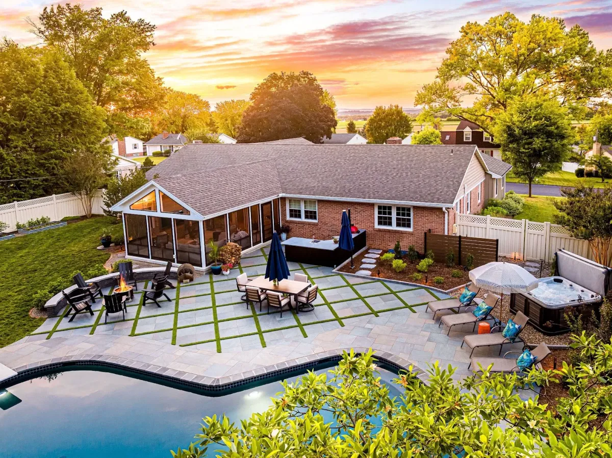 A custom stone patio with a pool and fire pit designed by a landscaper in Ambler, PA.