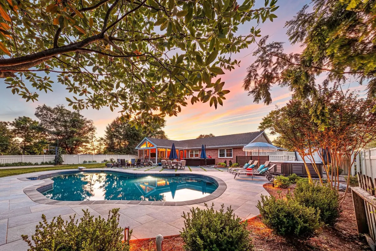 A luxury backyard pool and paver patio framed by trees, designed by a landscaper in Ambler, PA.