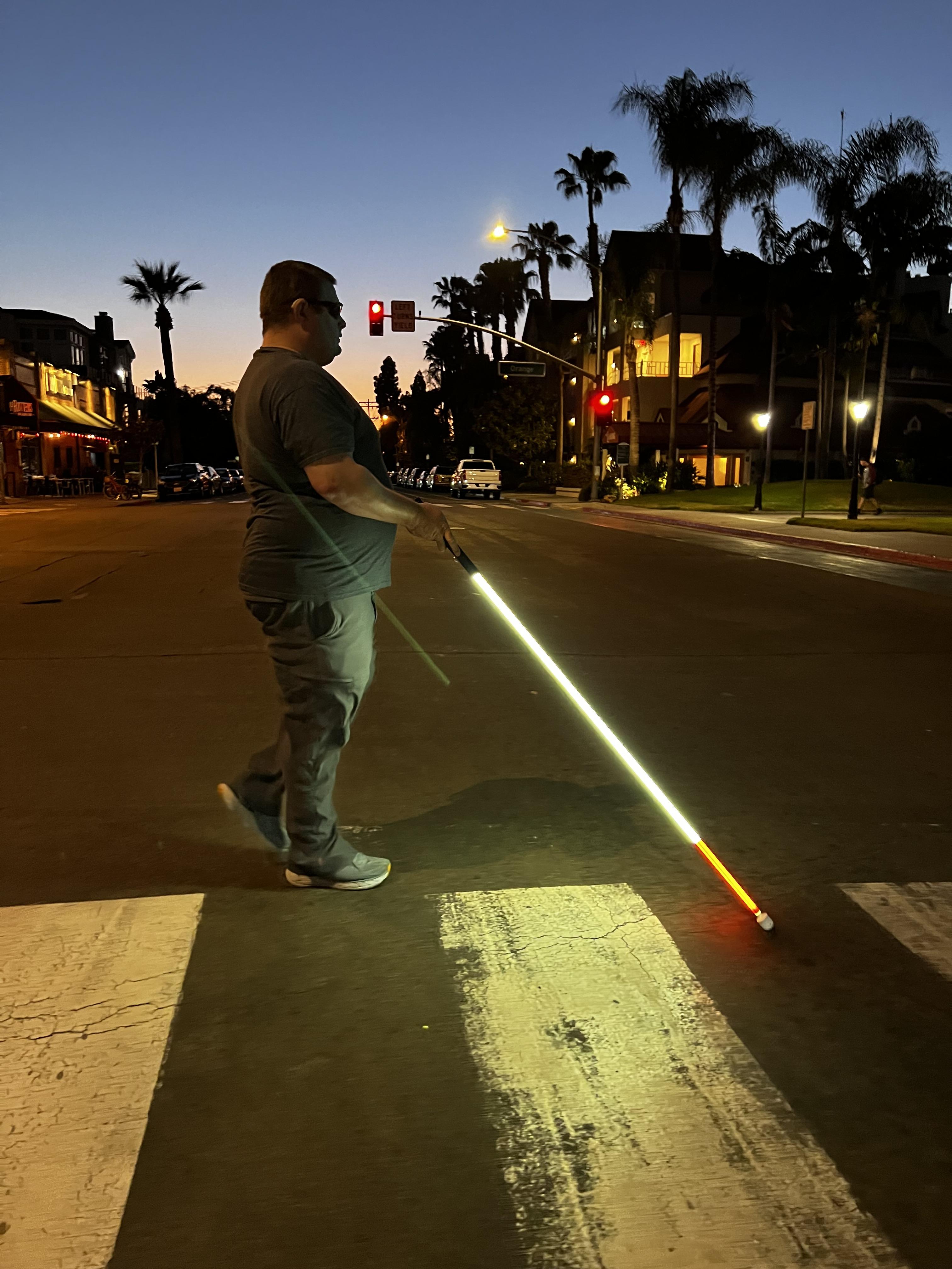 Lighted white cane glowing on pavement during a nighttime street crossing