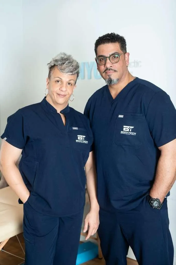 Elegant, sunlit wellness studio with navy and white decor, featuring a serene treatment table, soft natural light, and subtle greenery. The space feels premium, calm, and welcoming, with no people present, evoking a sense of tranquility and exclusivity.