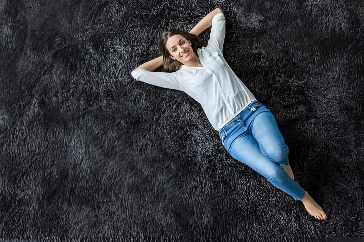 Image of a young woman lying on her back with her hands behind her back on a newly cleaned dark colored fluffy carpet