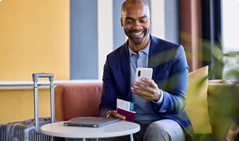 Smiling man looking at his smartphone while holding a passport and boarding pass
