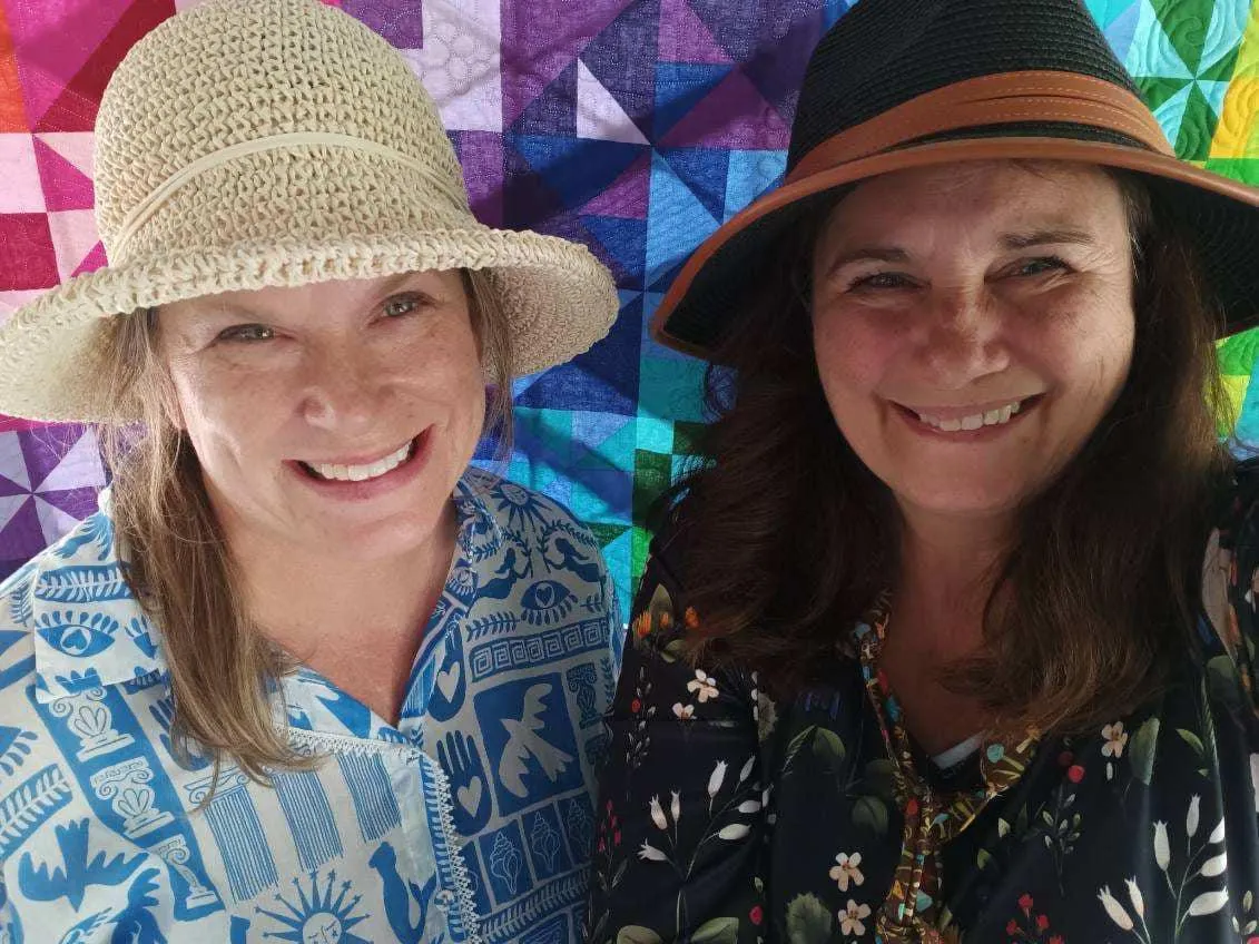 Barb and Corinne standing in front of a quilt smiling