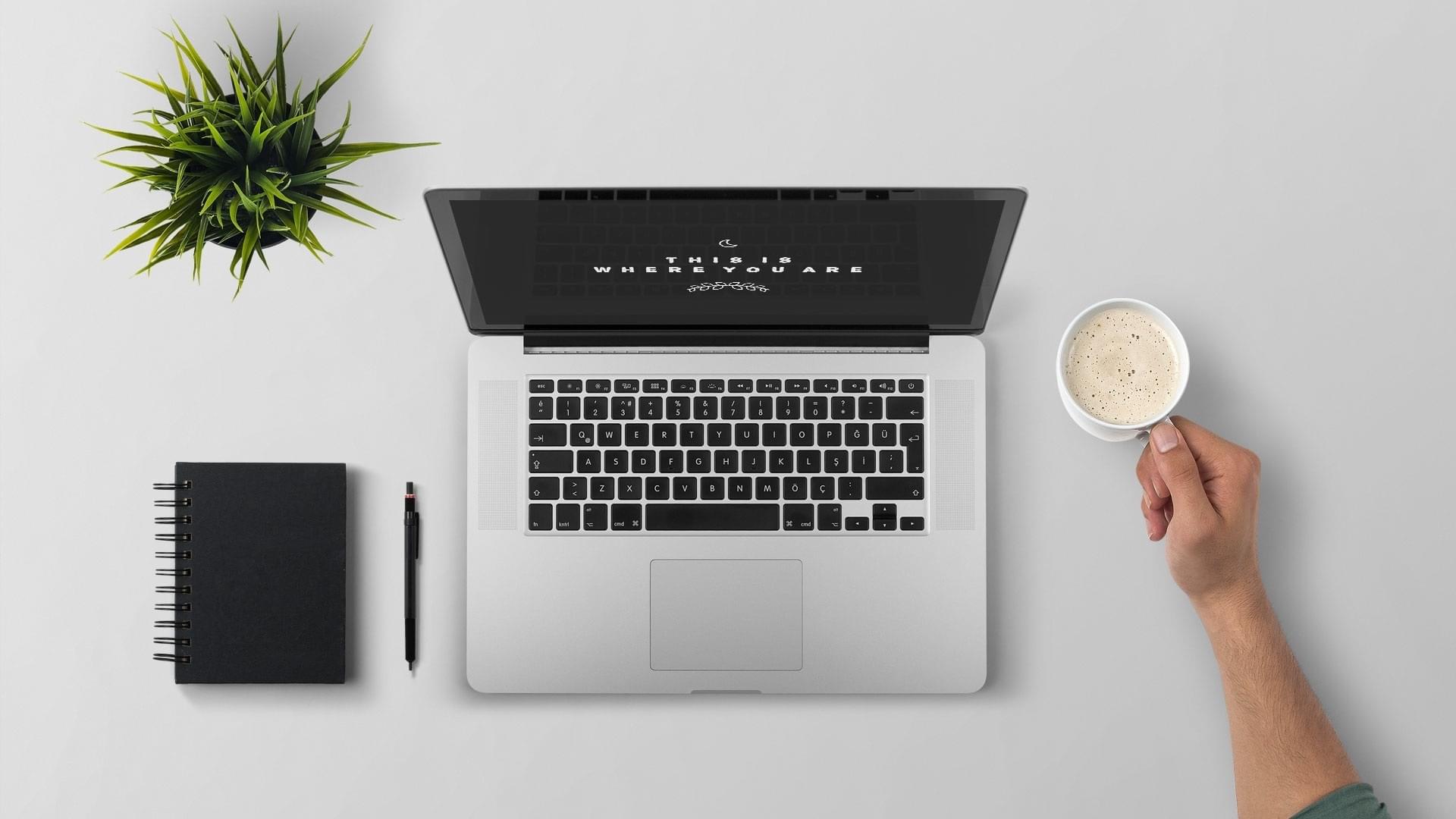 Laptop, a plant, a notepad and a cup of coffee on a desk depicting professional resume writing for engineers