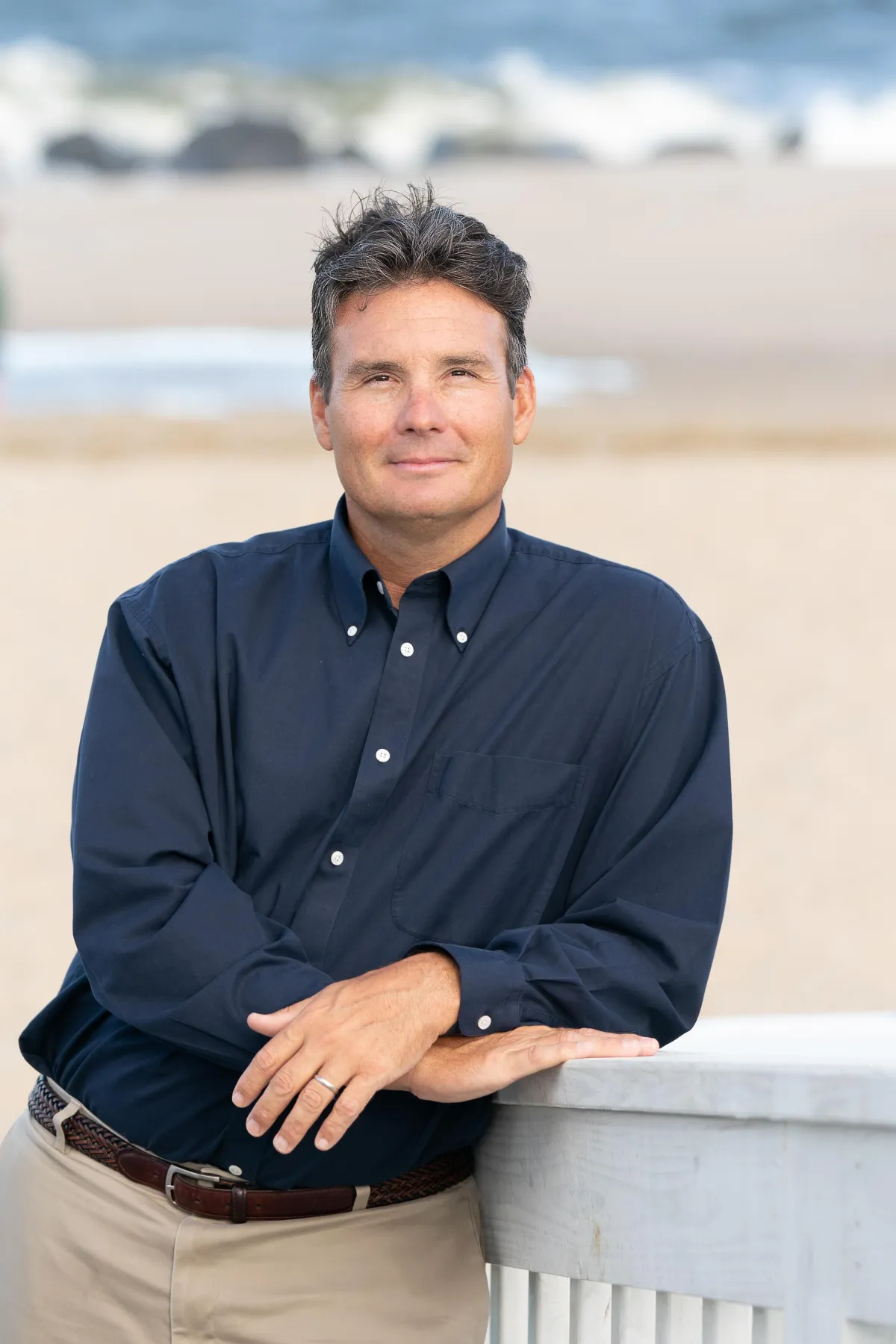 Portrait of a man smiling, wearing a dark blue dress shirt with arms crossed, standing outdoors.