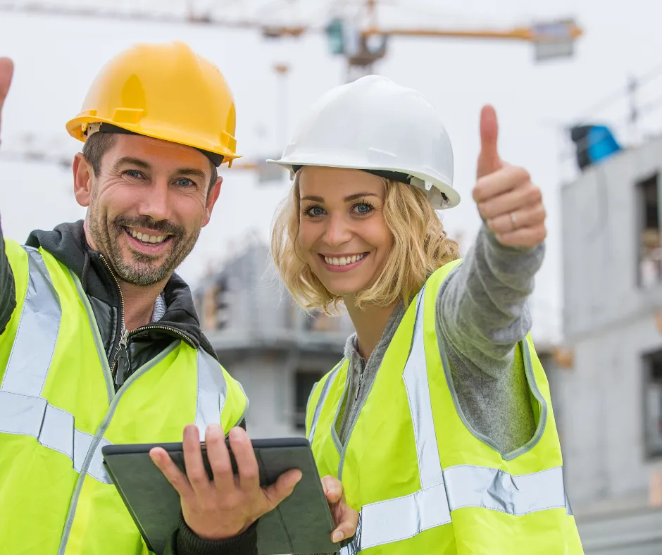 A construction site duo in safety gear, one giving a thumbs up and the other holding a tablet.