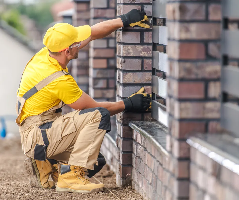 A construction worker in a yellow shirt and gloves carefully adjusts bricks on a wall.