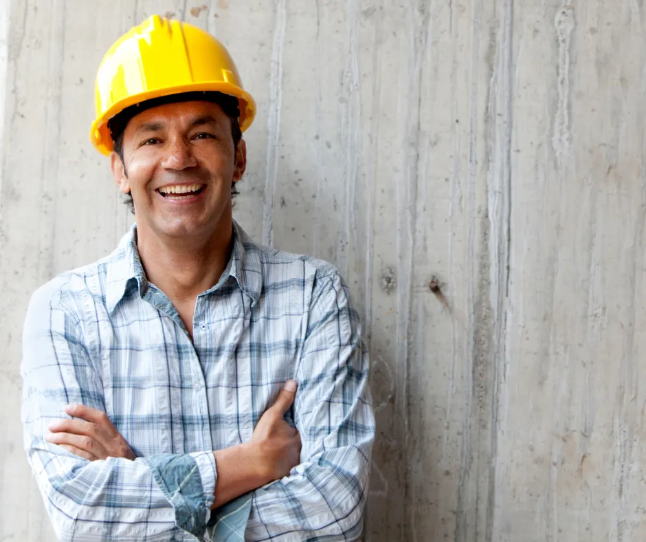 A construction worker wearing a yellow hard hat and a plaid shirt stands confidently.