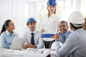 A group of professionals in hard hats engaged in a meeting, with one individual presenting information to the team.