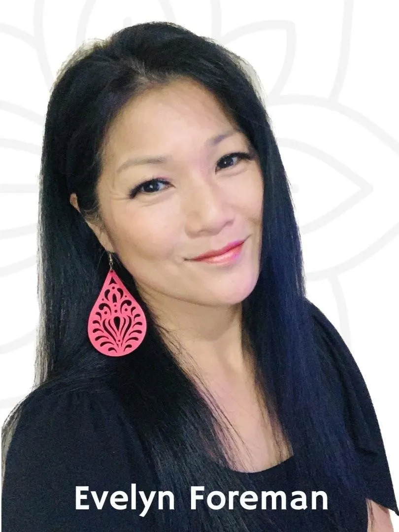 Evelyn foreman with long, dark hair and pink earrings stands against a light