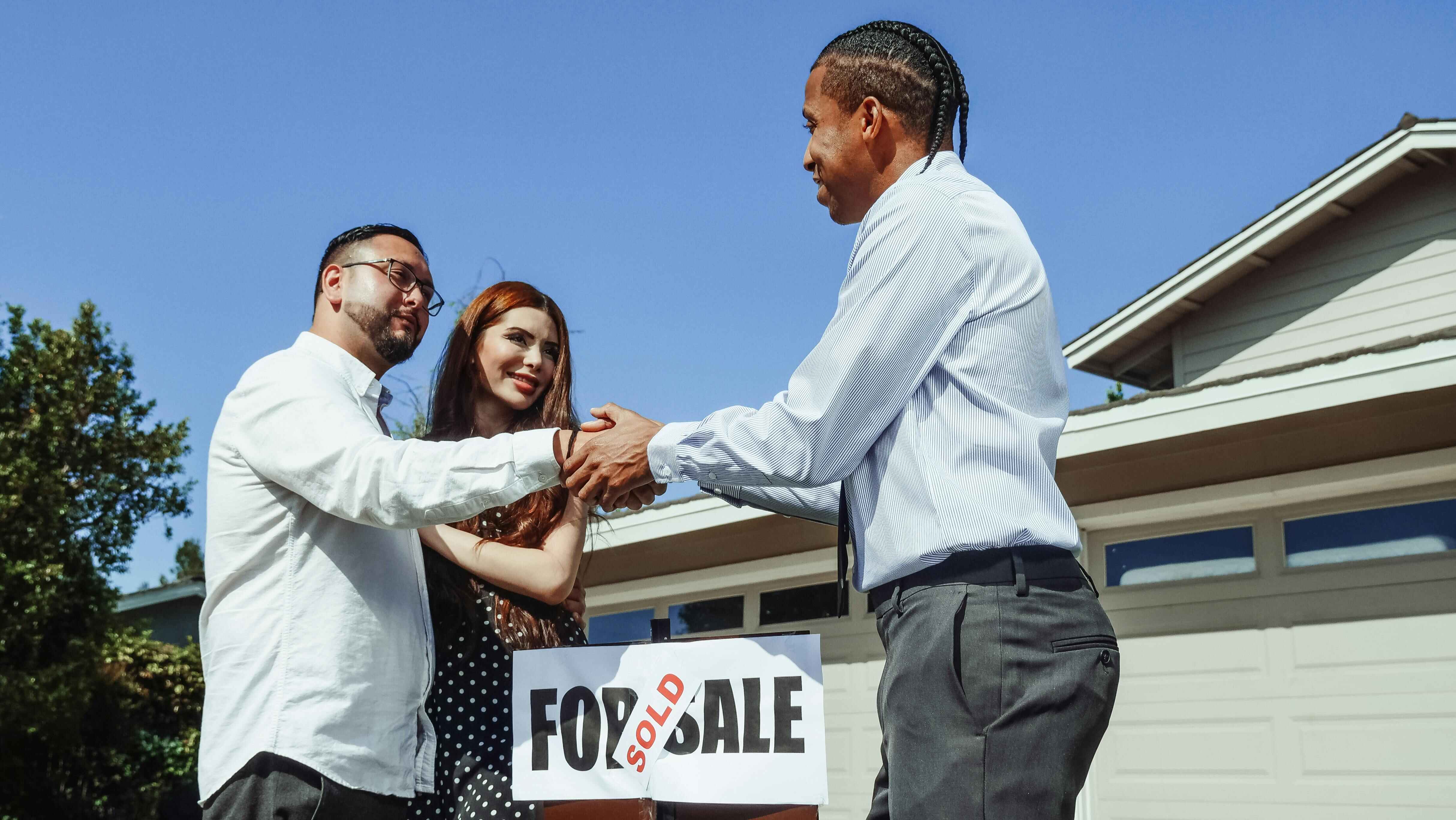 Wollongong buyer's agent congratulating a couple after successfully purchasing a home, with a SOLD sign visible in front of the property.