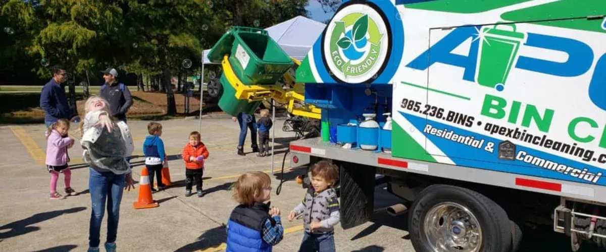 Excited children playing with bubbles near an Apex Bin Cleaning truck with a green eco-friendly bin in operation.