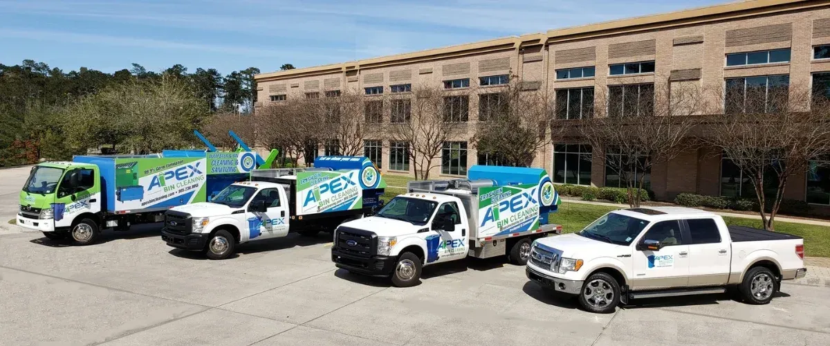 A fleet of three Apex Bin Cleaning service trucks and a pickup truck parked in front of a modern office building.