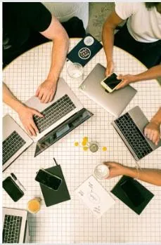 3 people working at a table with laptops 