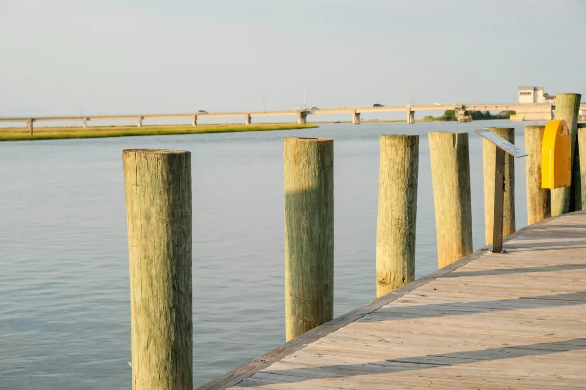 Wooden dock on tall round timber pilings beside calm water and a strip of marsh