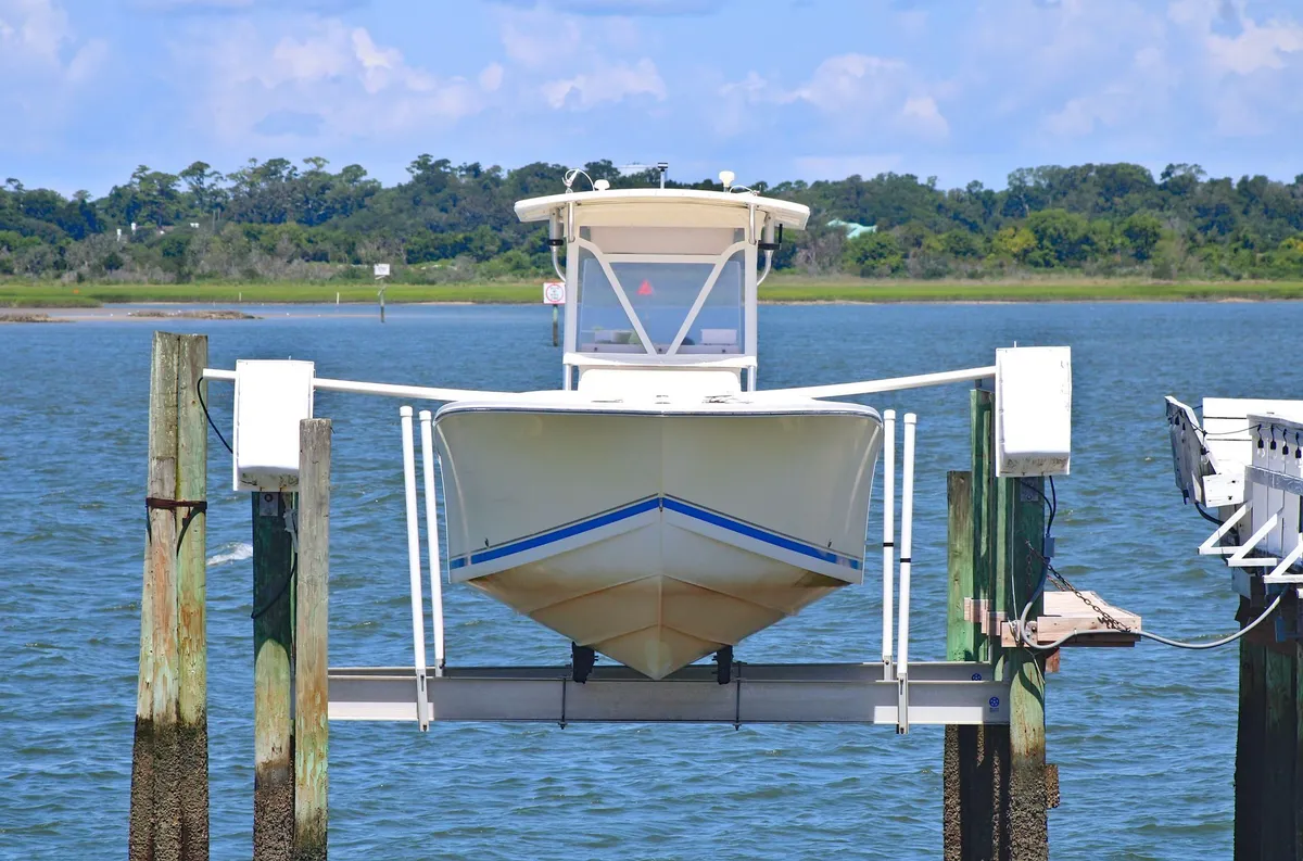 White center-console boat raised out of the water on a boat lift beside dock pilings