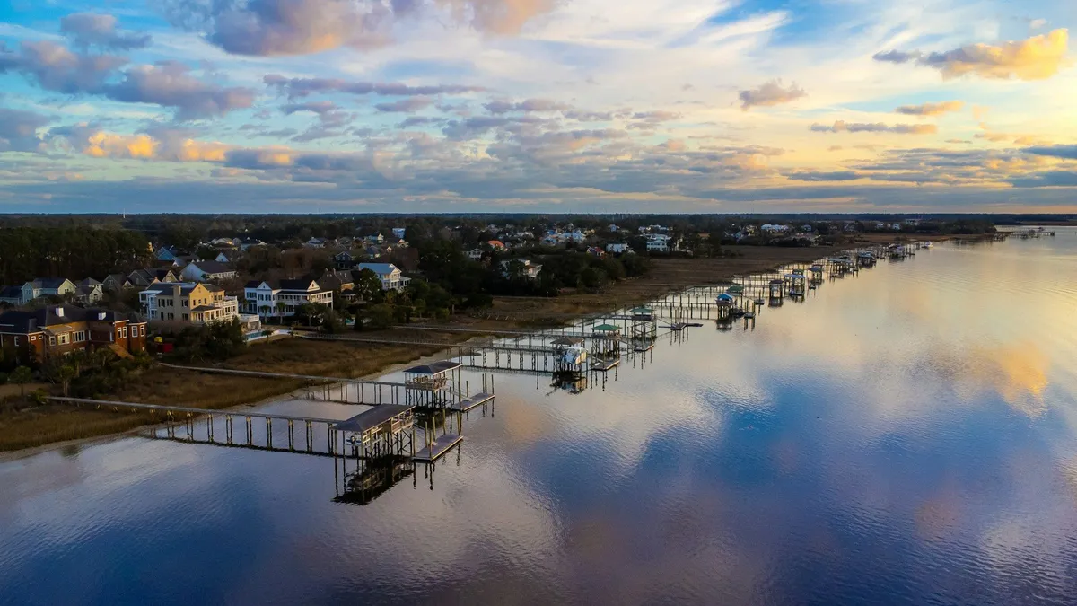Aerial view at sunset of homes with long private docks crossing marsh to still water