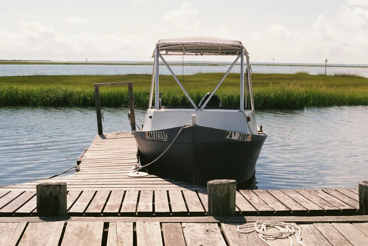 Small canopy boat tied to the end of a wooden dock, with green marsh grass across the water