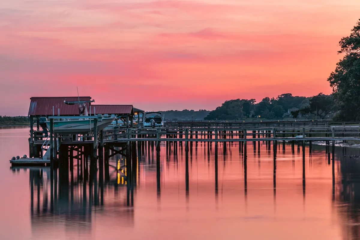 Wooden dock and boathouse on pilings against a pink and orange sunset