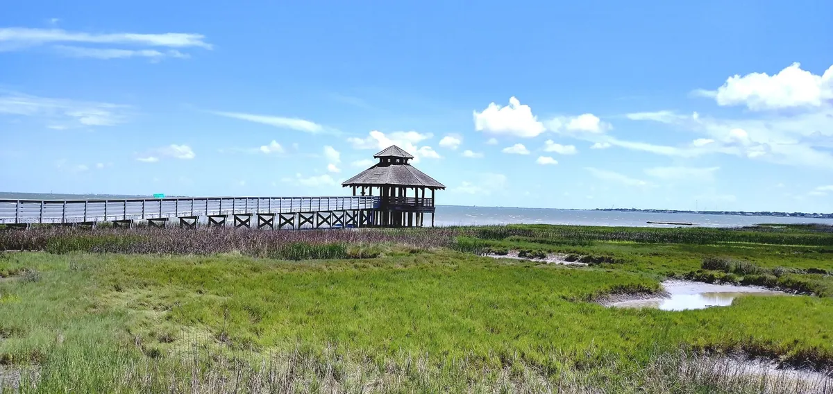 Long wooden pier over green marsh grass ending at a gazebo by the water