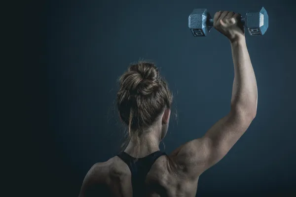 A woman lifting a dumbbell overhead, viewed from behind, representing the strength training that supports muscle mass during perimenopause.