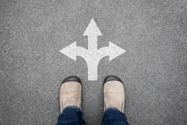 A pair of shoes facing a three-way path marked on pavement, representing the choice between different directions.