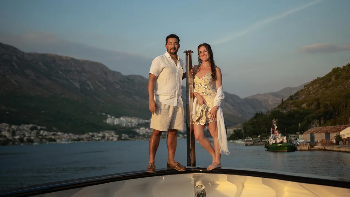 Couple enjoying a yacht journey with a mountain-lined harbour in the background