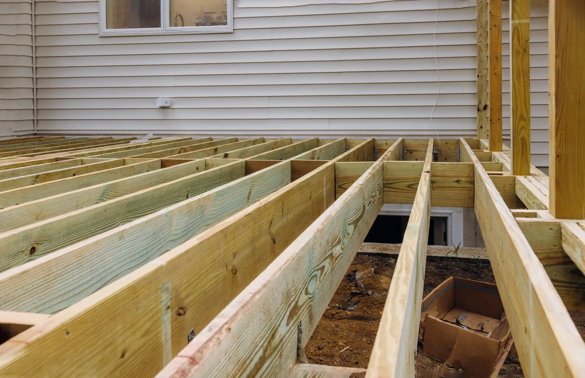 Wooden deck under construction with exposed beams and joists attached to the side of a house.