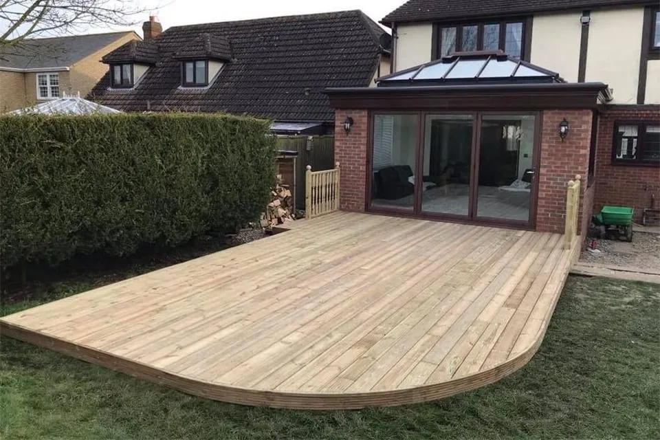 Backyard wooden deck with smooth, curved edges extending from a house with large glass doors